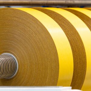 Mehrere große gelbe Klebebandrollen auf einer Metallwelle in der industriellen Fertigung.