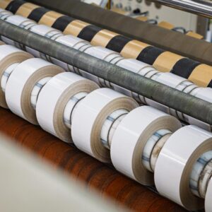 Mehrere weiße Klebebandrollen auf einer industriellen Schneid- und Wickelanlage.