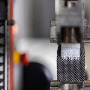 Nahaufnahme eines schwarzen Materialstreifens während der Bearbeitung in einer industriellen Prüfmaschine.