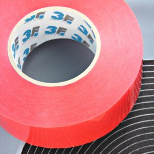 Nahaufnahme einer großen roten Klebebandrolle auf einer schwarzen Materialoberfläche.